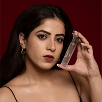 Female model holding Roméo by Tsar 20 ml perfume bottle against a deep red studio background
