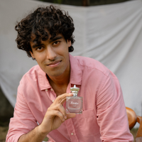 Male model holding Zeste by Tsar 100 ml perfume bottle in an outdoor lifestyle setting with a neutral fabric backdrop
