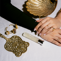 XVIII Oud by Tsar 20 ml perfume bottle styled with gold accessories and hands on a white background
