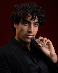Male model holding Roméo by Tsar 20 ml perfume bottle against a dark studio background